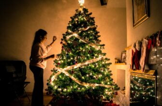 child standing in front of Christmas tree with string lights
